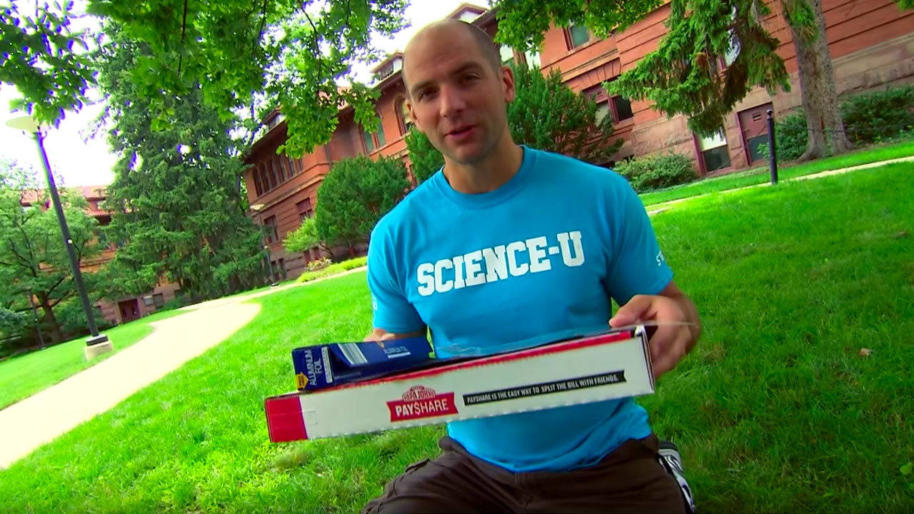 Instructor holding a pizza box, aluminum foil, and other items to make a solar oven