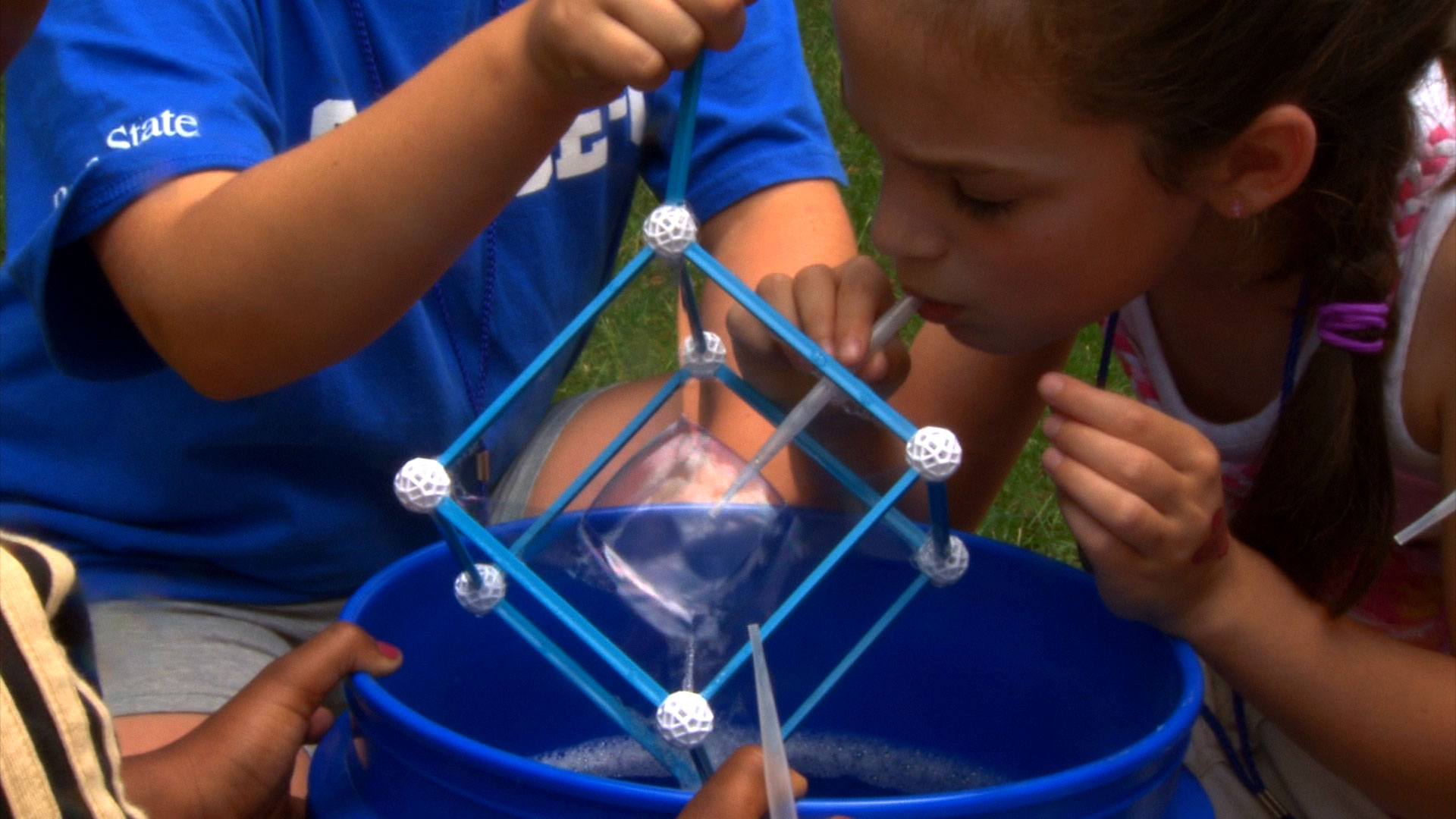 Young girl attempting to blow a bubble in a square frame