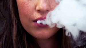 Close up of younger woman blowing vape smoke out of her mouth.