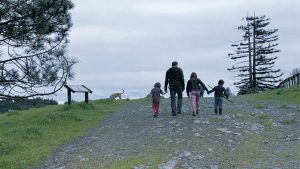 A man, three children, and a dog walking along a gravel path.