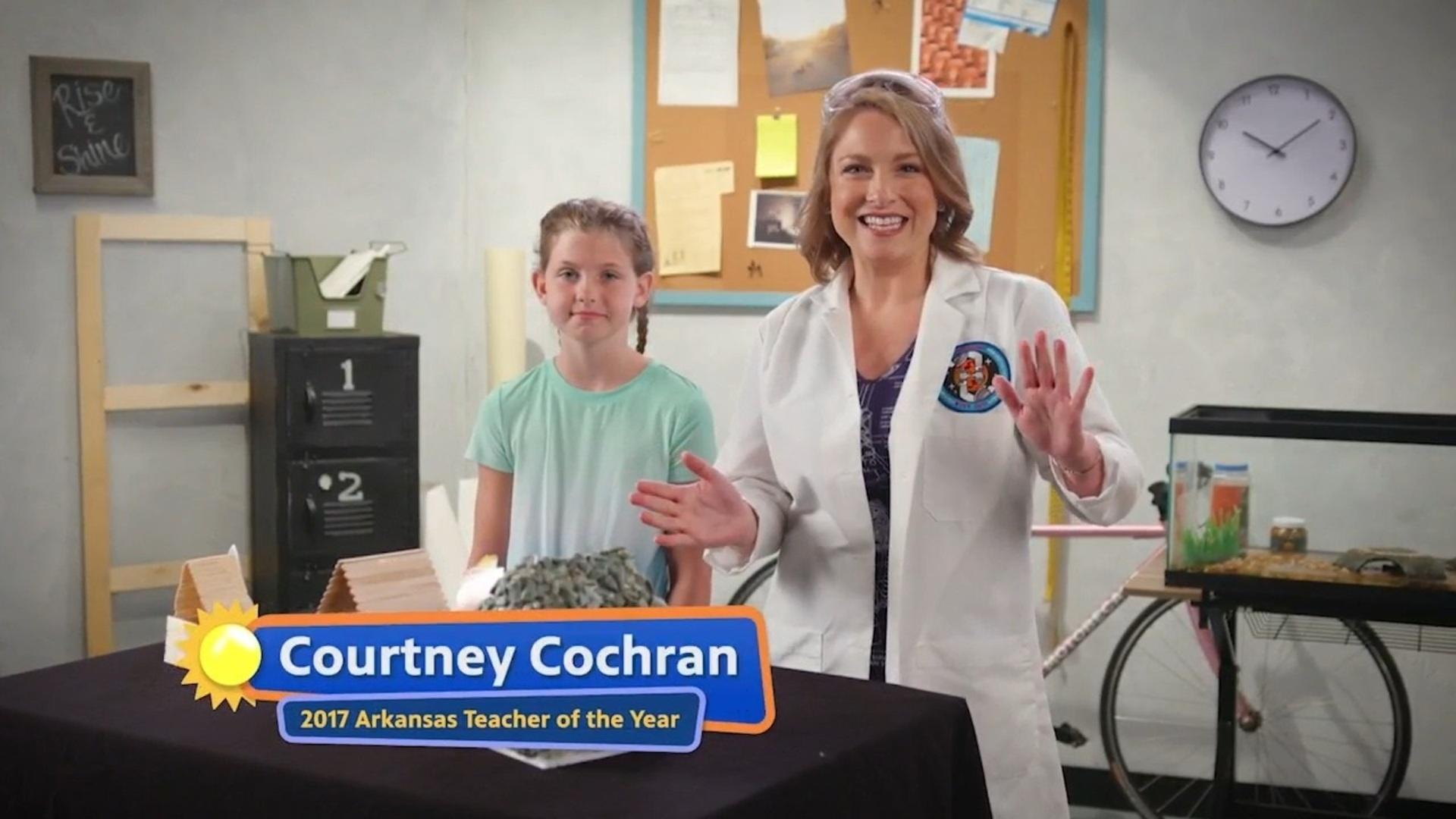 A woman dressed in a white laboratory coat stands next to a girl