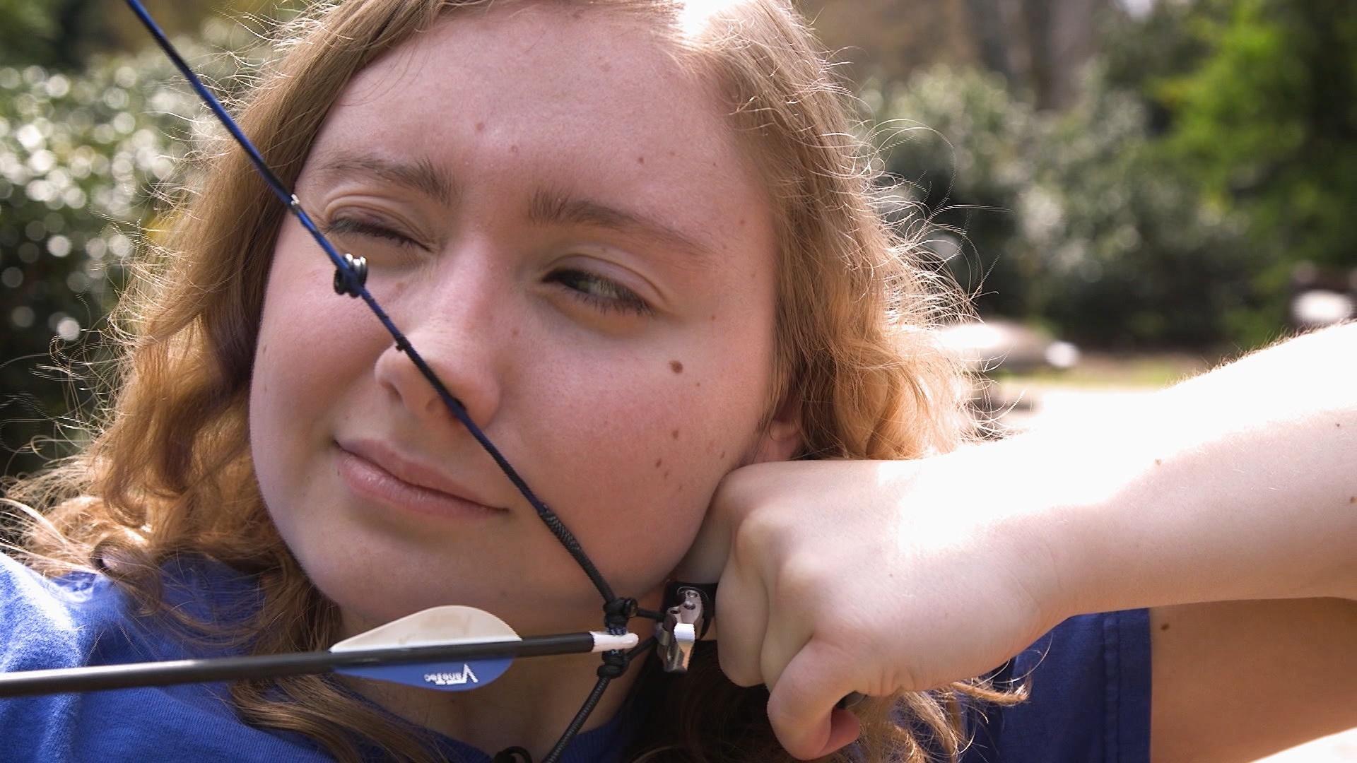 A girl pulling back a bow and arrow.