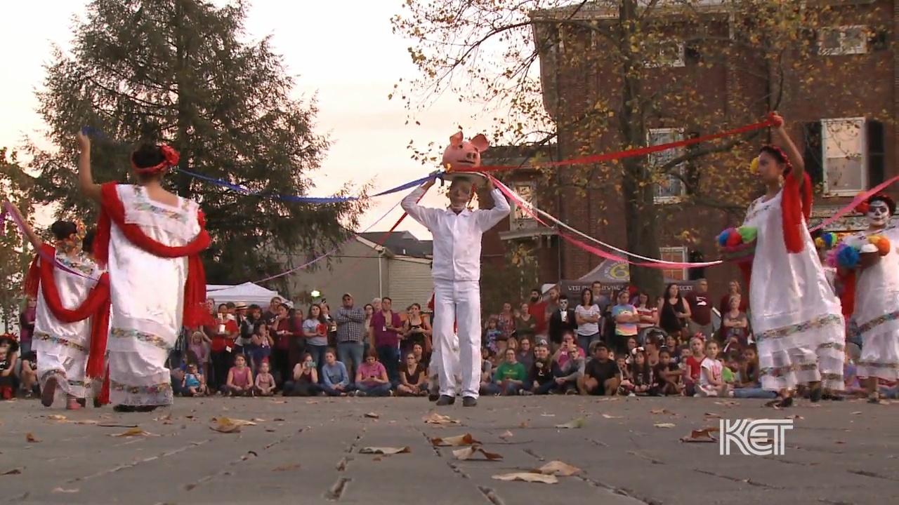 A man holding a fake pig head while four women dance around him.