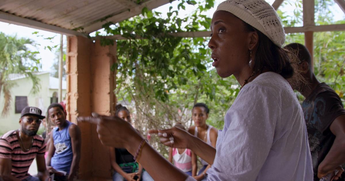 A woman in a white shirt and hat talking to a group of people.