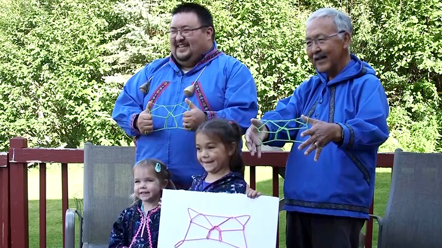 Two men and two children standing together with rope cat's cradles.