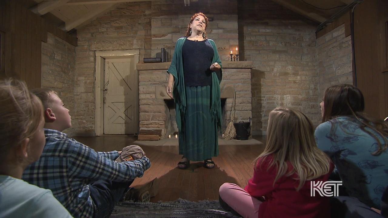 A standing woman presenting to several sitting children.