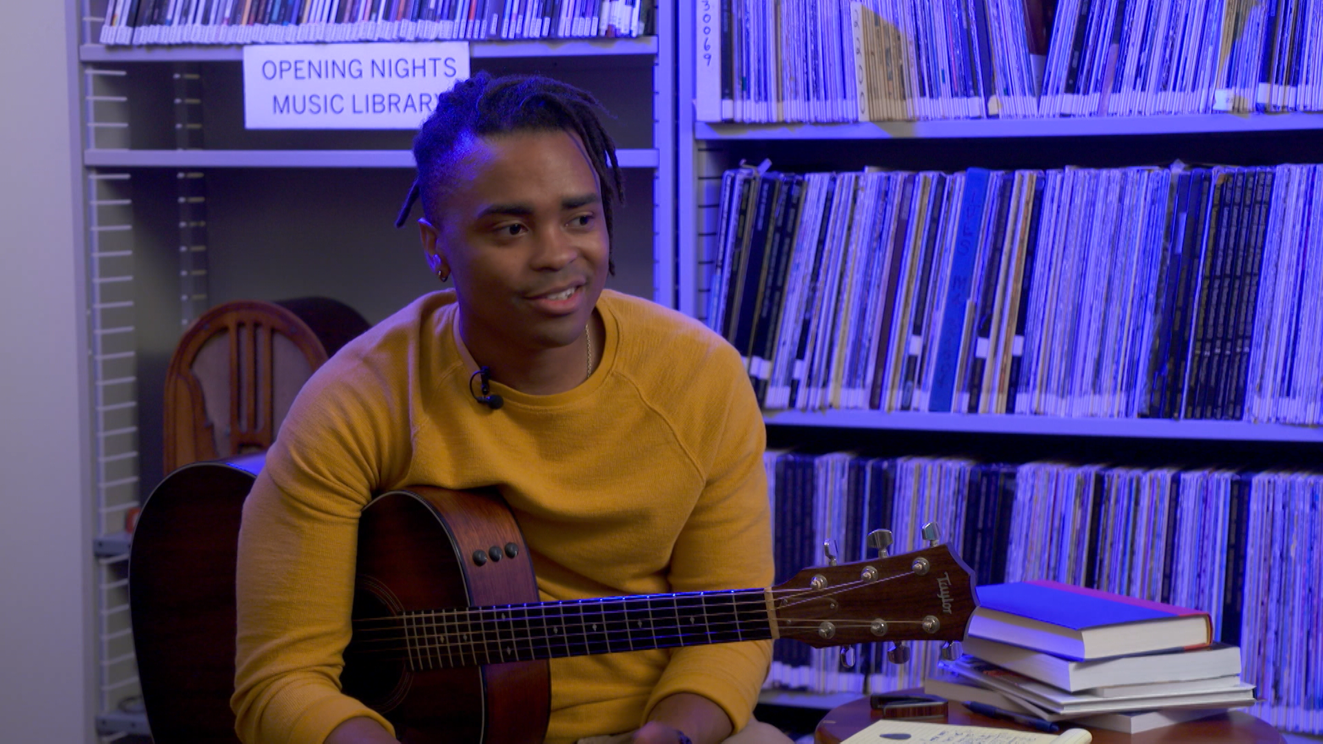 Royce Lovett holding a guitar in front of shelves of record albums.