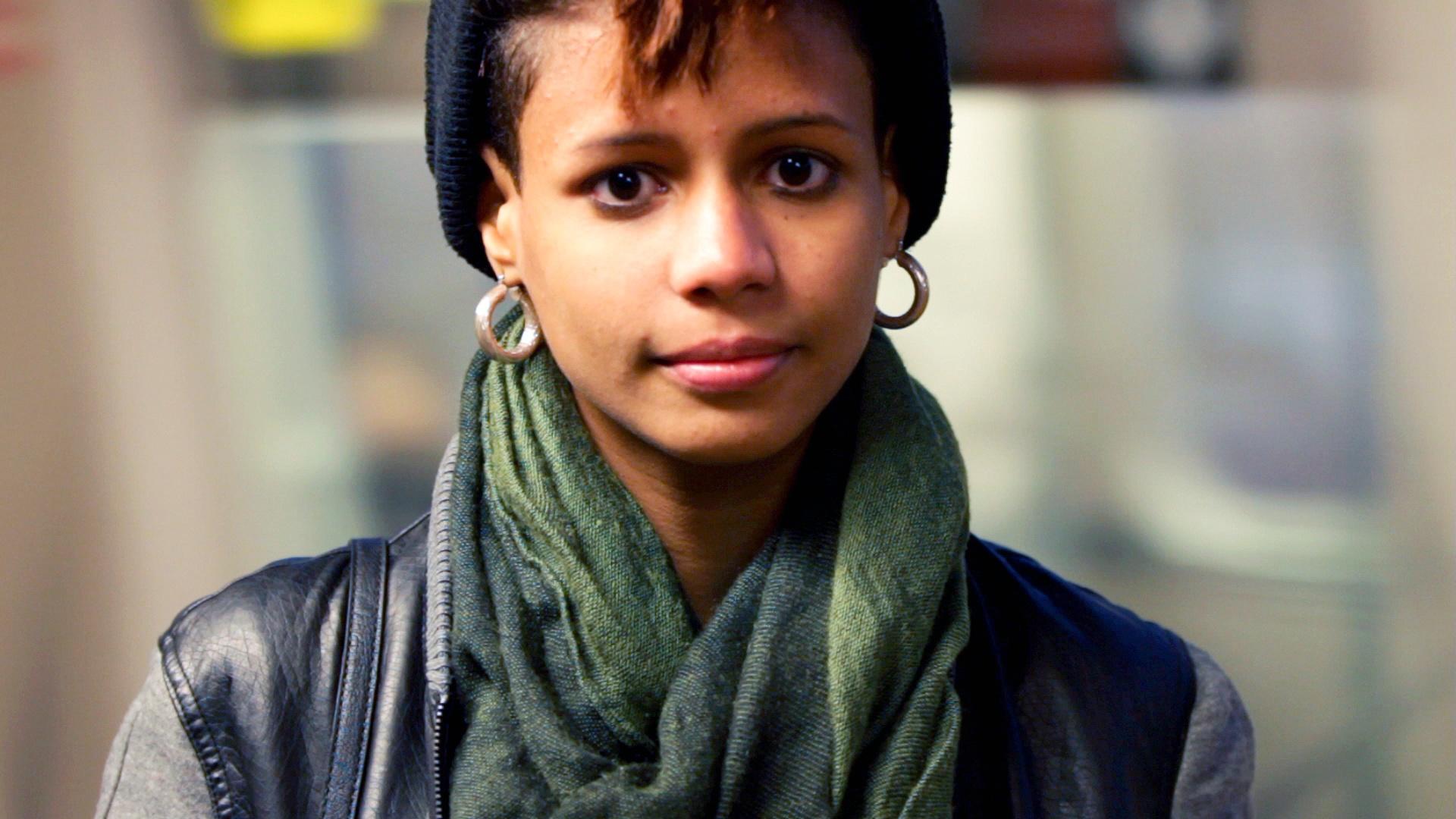 A woman in a scarf and hat looking into the camera.