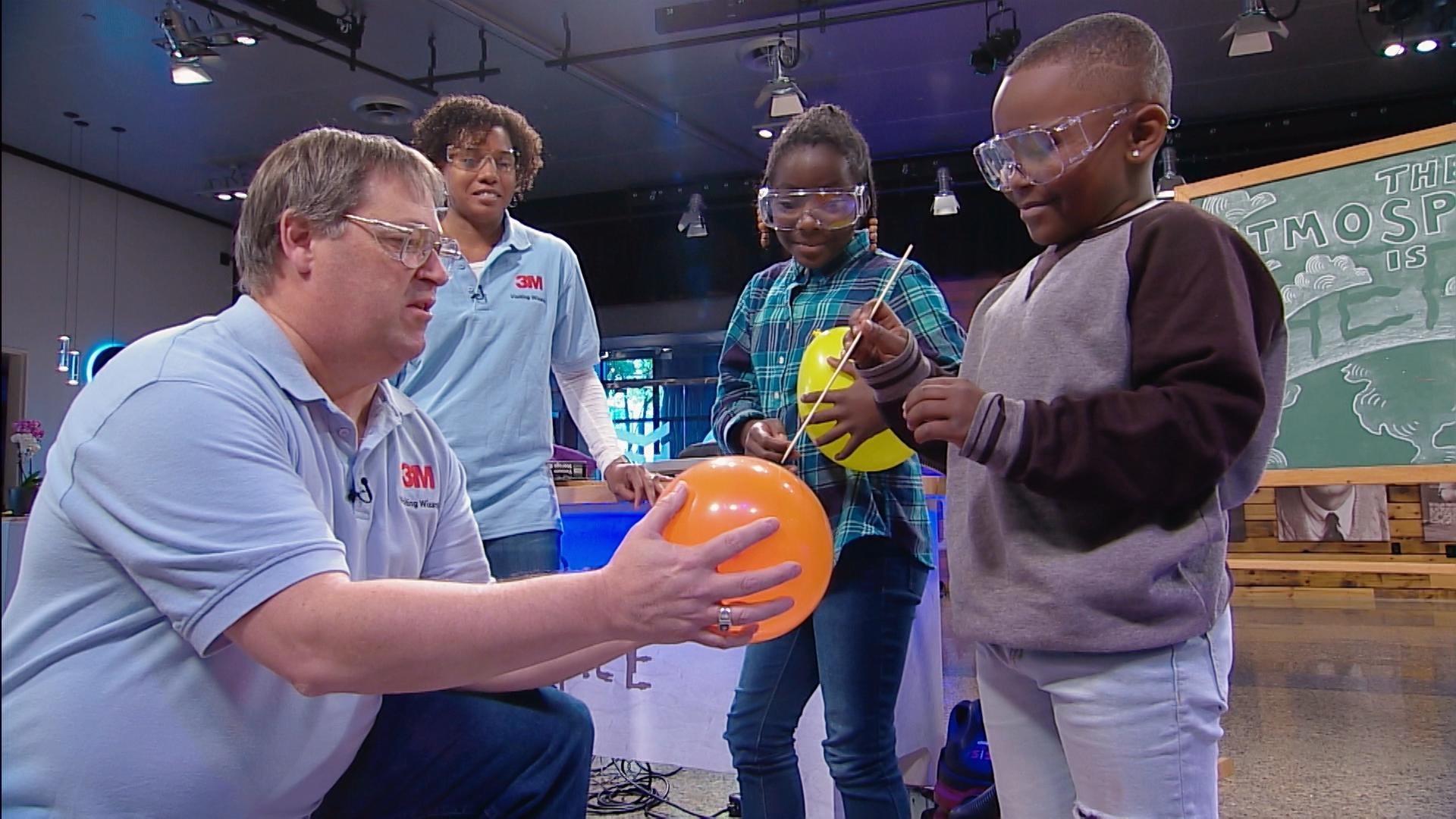 An adult holds a balloon while a child pops it.
