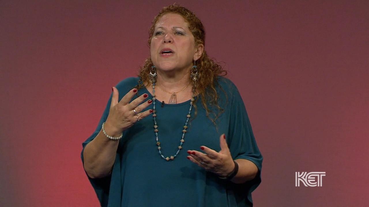 A woman in a blue shirt telling a story and gesticulating.