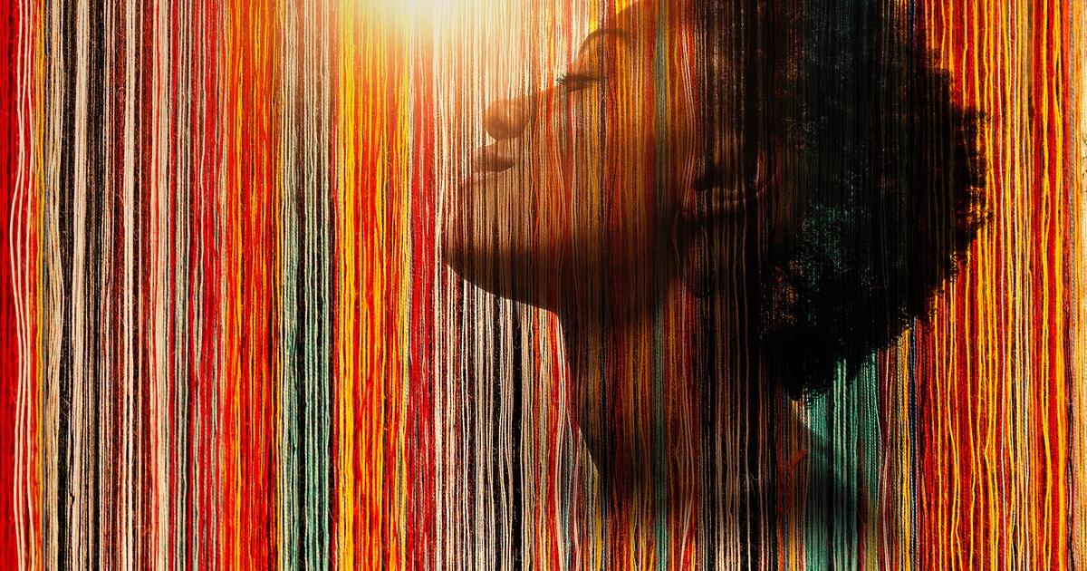 A black woman behind multi-colored threads.