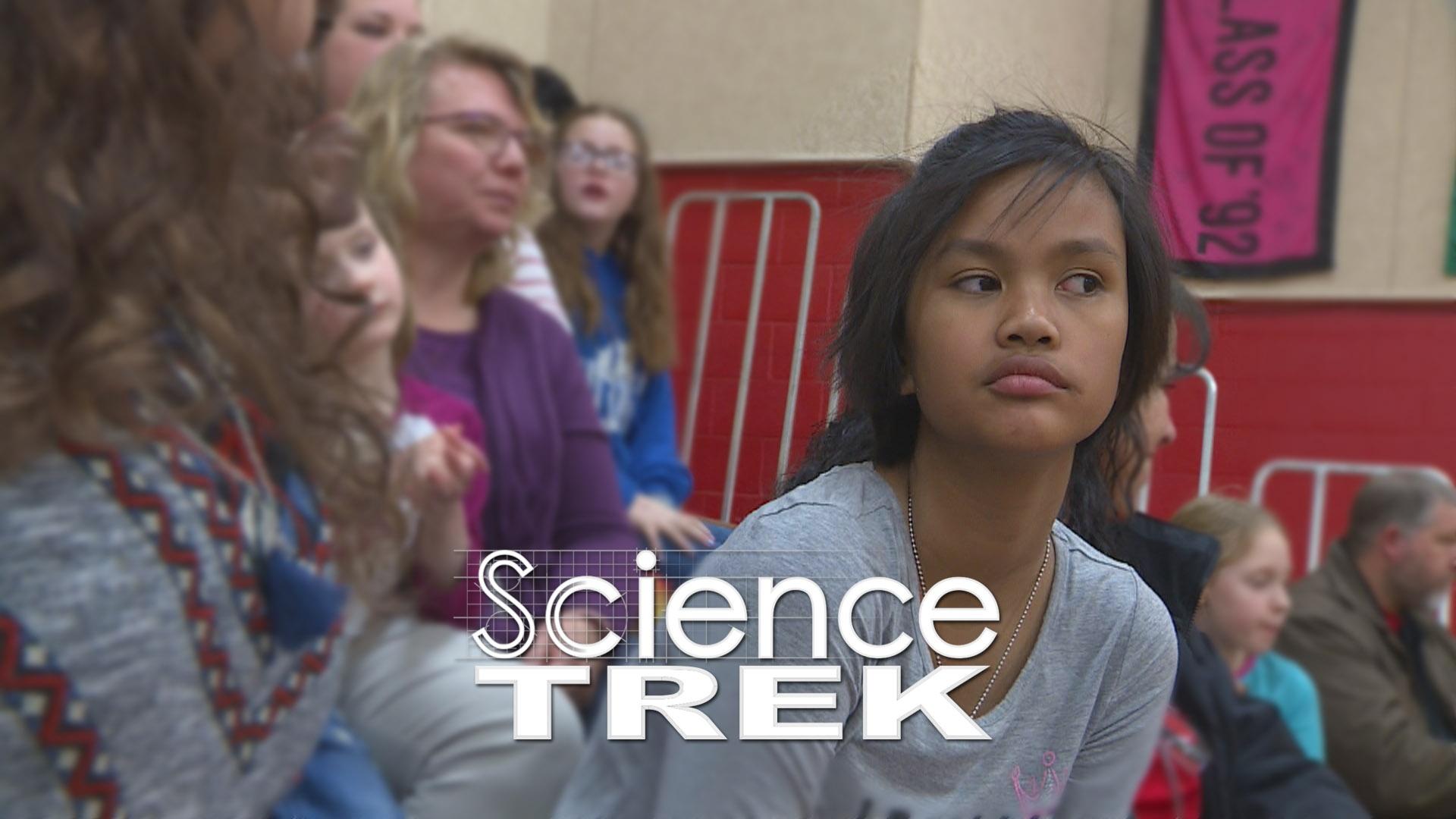 A woman leaning forward to listen in bleachers surrounded by other people.