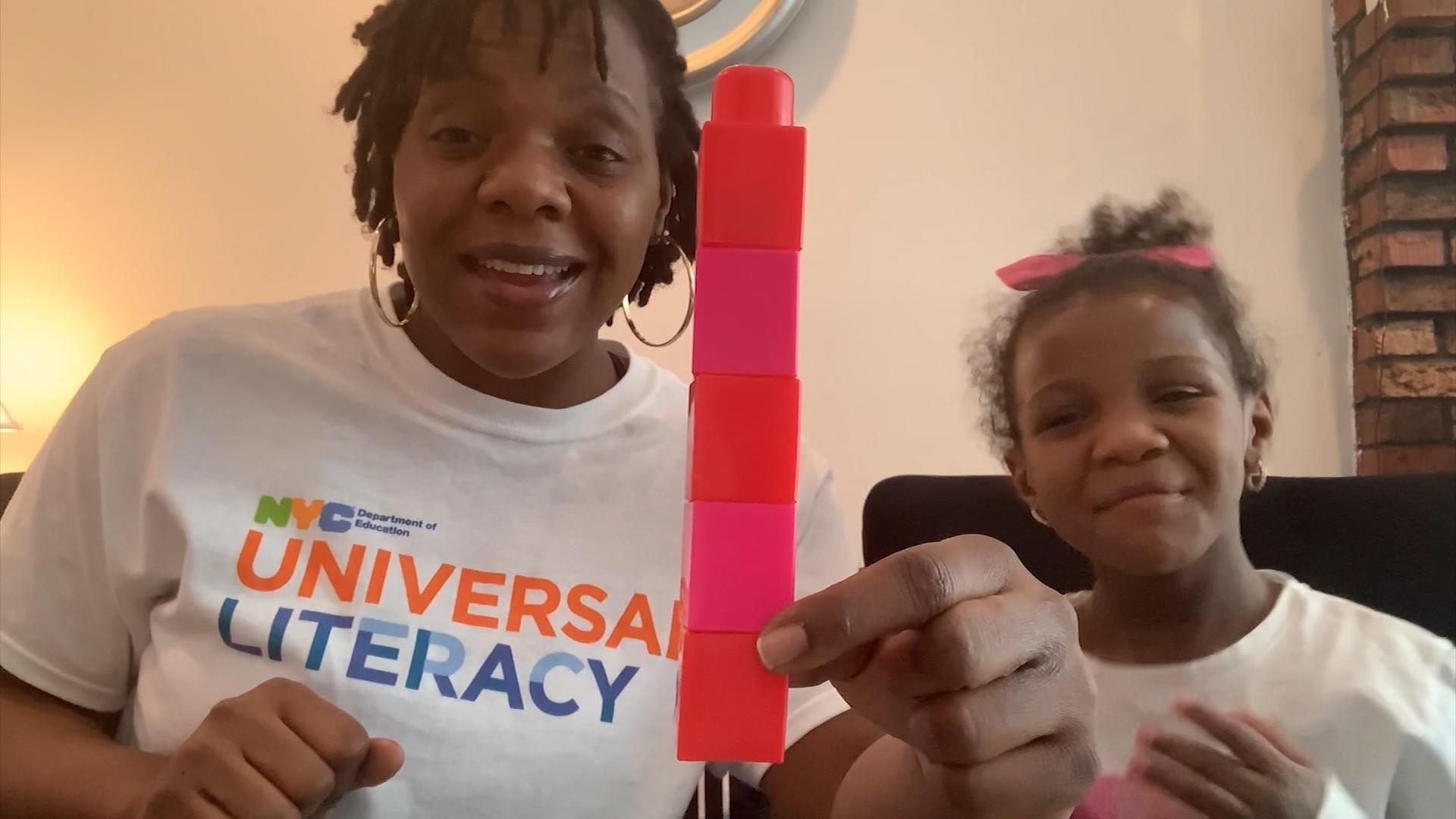 A black woman and girl holding a stack of blocks.