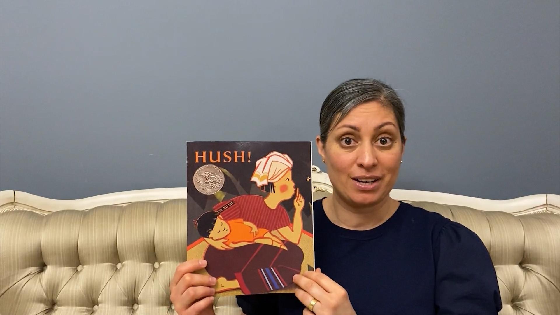 A woman sitting on a couch holding up a book.