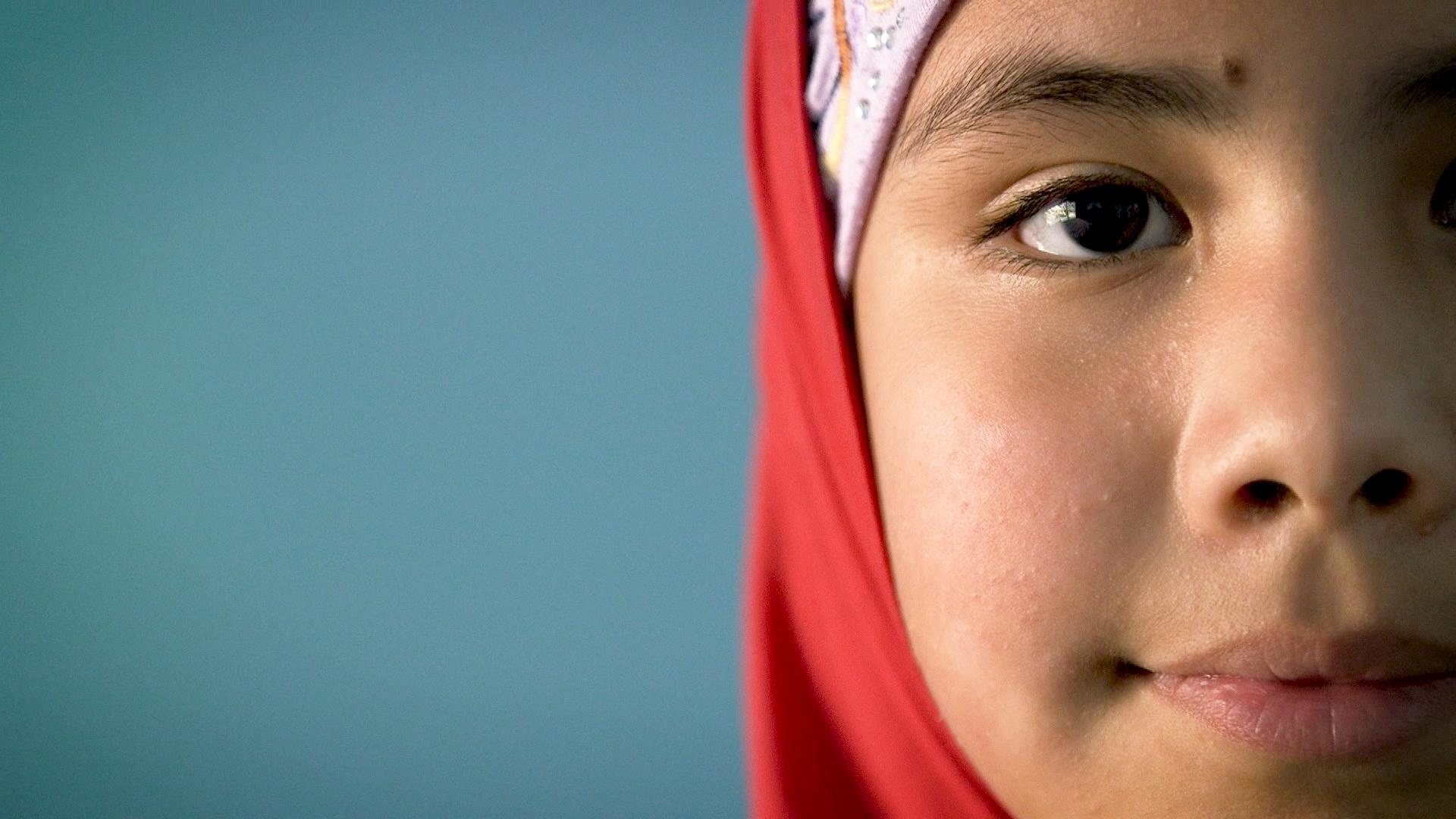 An girl in a red headscarf looks at the camera.