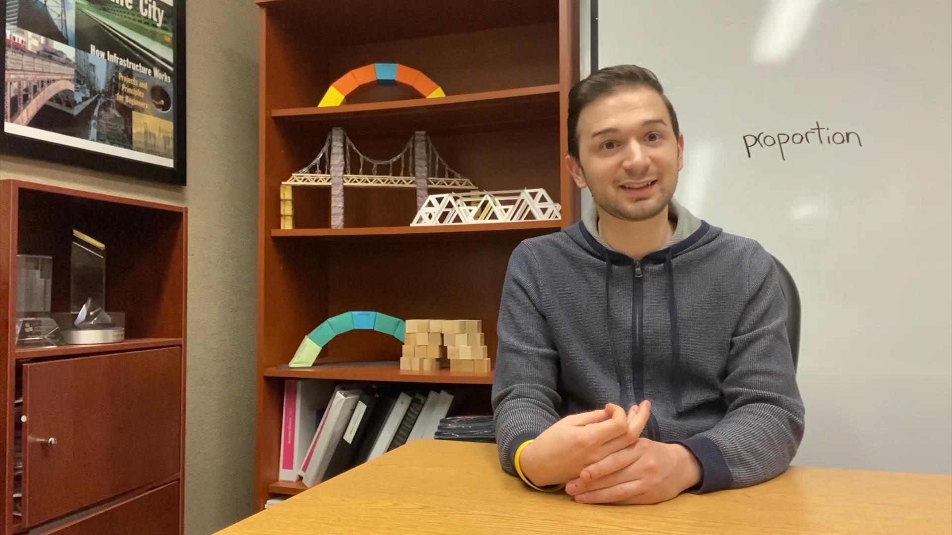 A man sits at a table in front of a whiteboard.