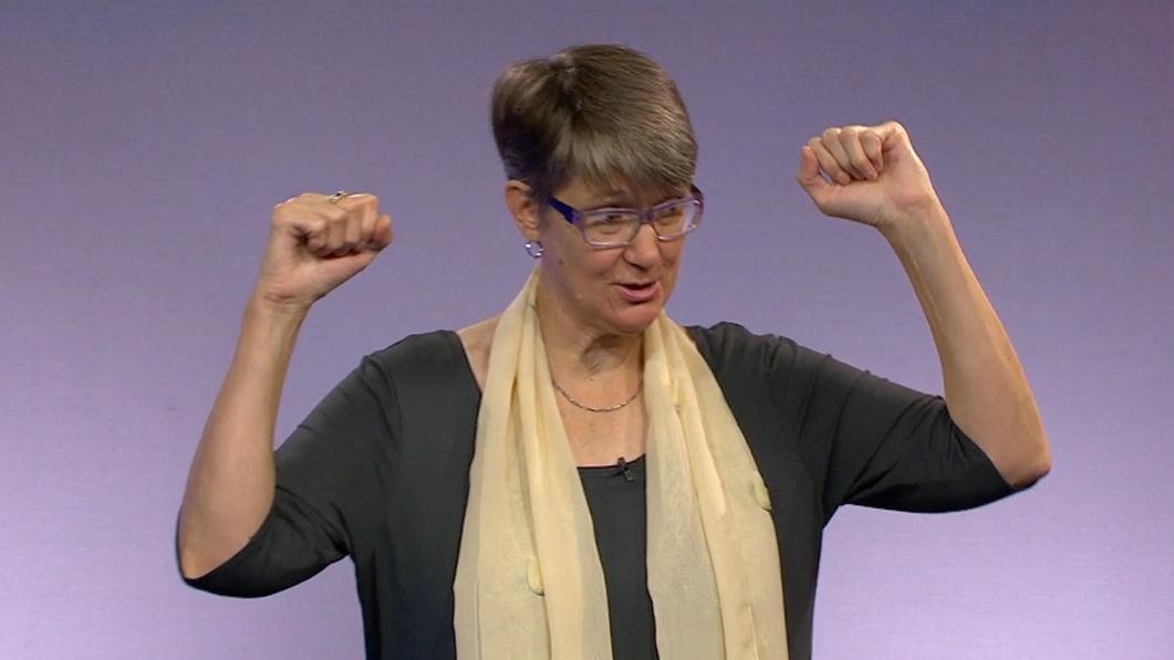 A woman with a scarf hold her hands up next to her head.
