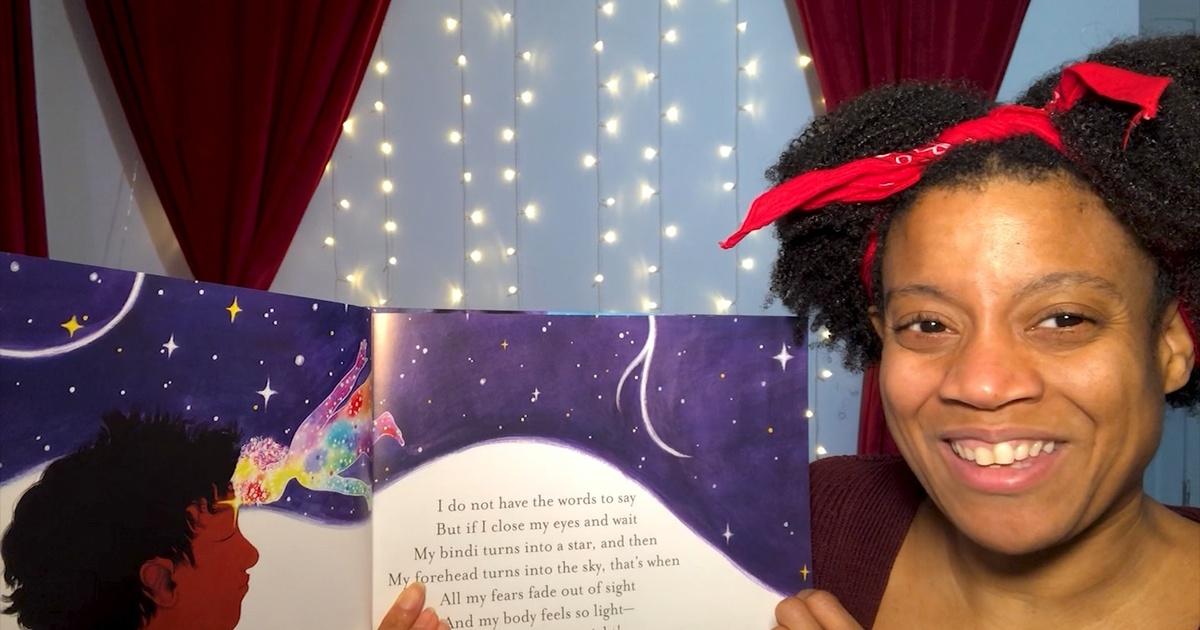 A woman with a red scarf in her hair holds a book open to the camera.