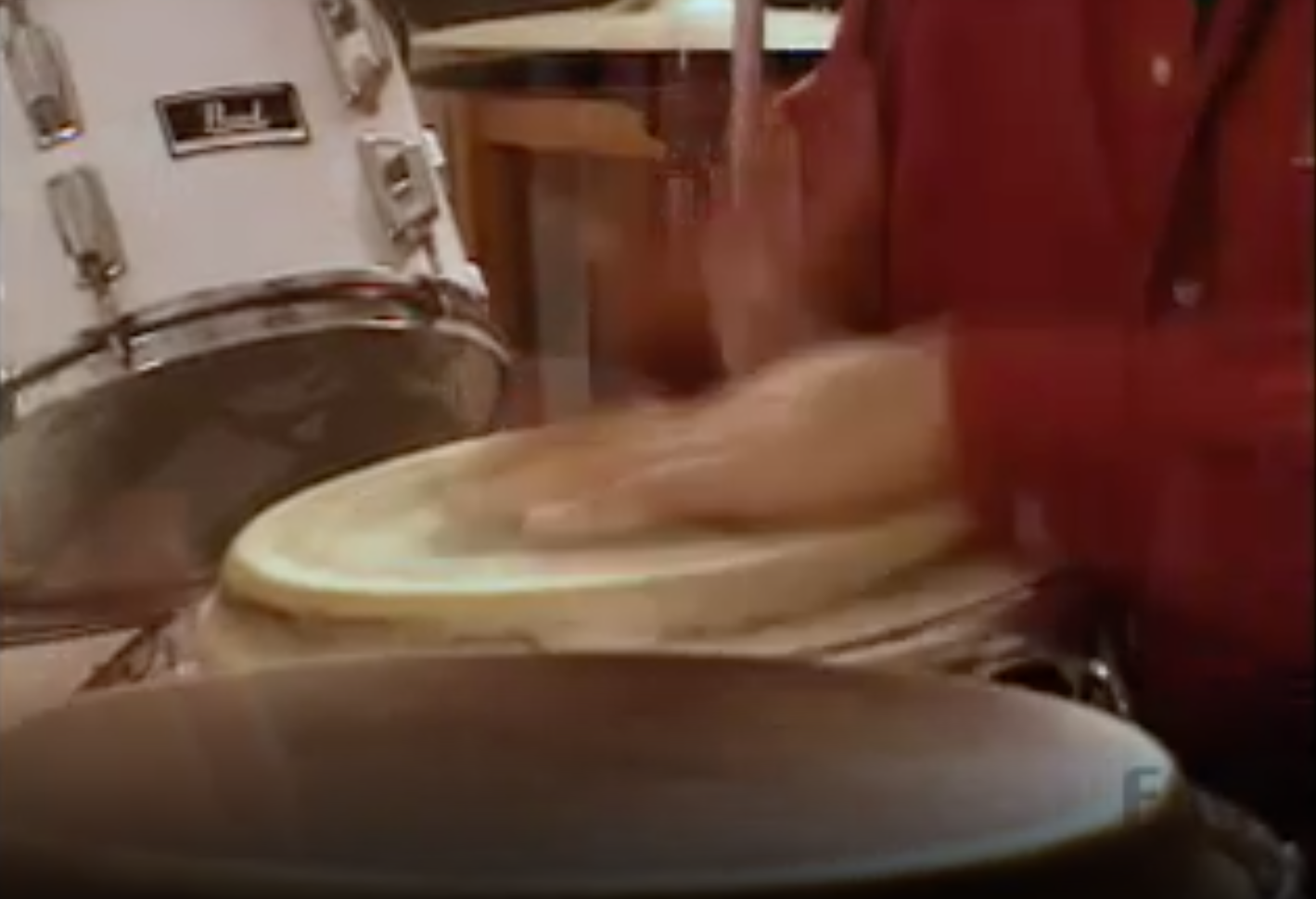 A man in a red shirt plays on a conga.