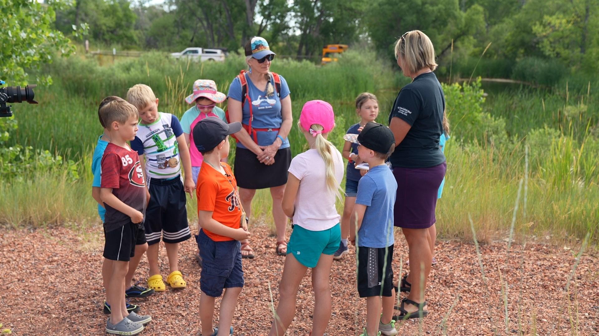 A group of small children and two adult women stand together talking.