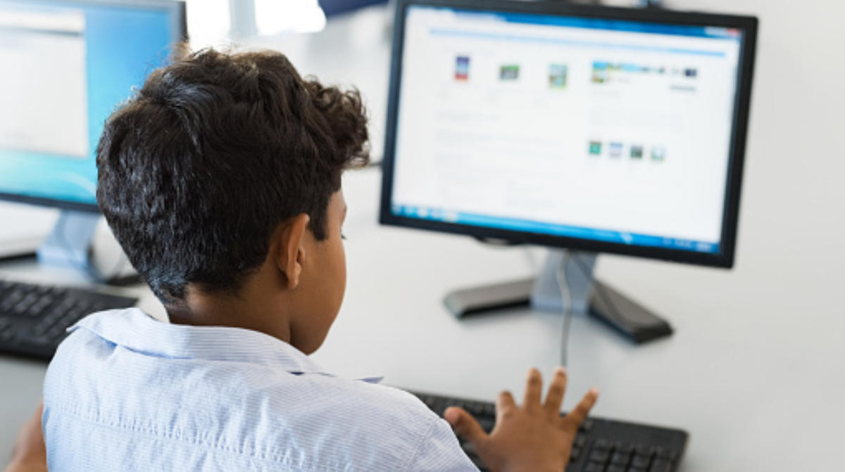 A student with dark hair sits in front of a computer typing on a keyboard.