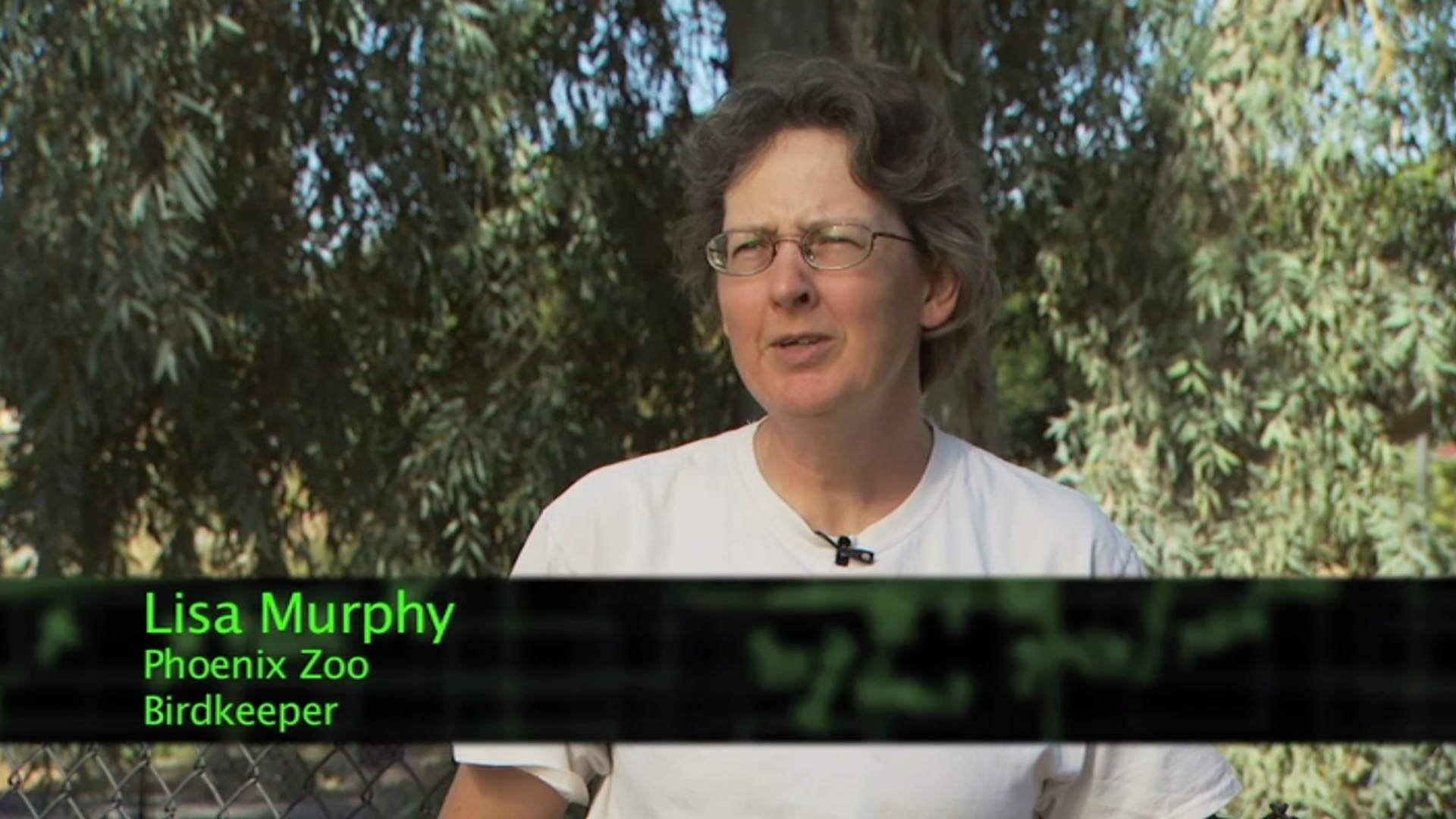 a White woman in a white shirt sits in front of trees.