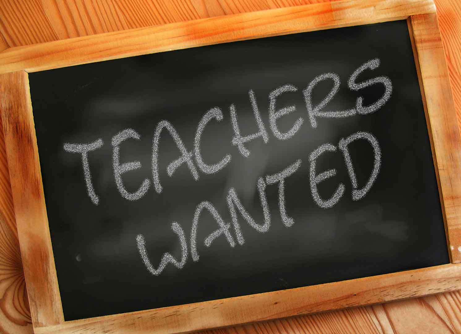 A chalkboard with the worlds TEACHERS WANTED written on it.
