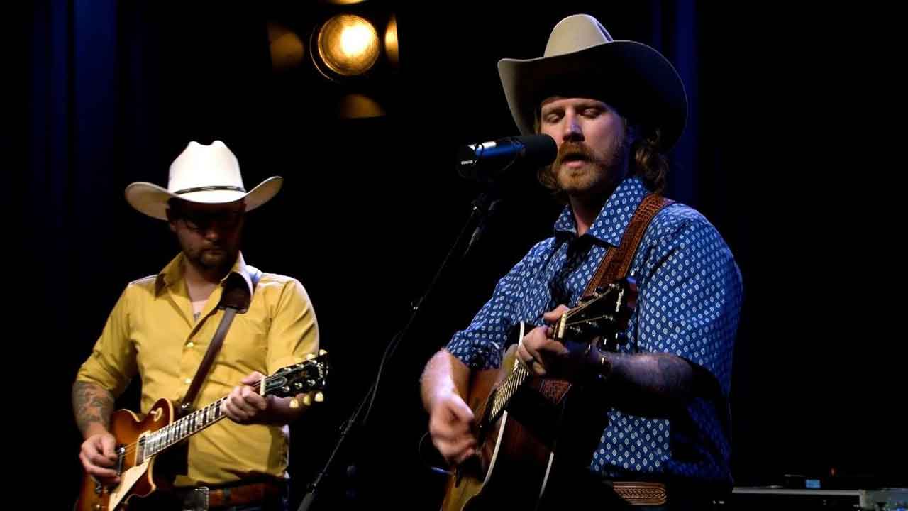 Two men wearing cowboy hats and playing guitars.