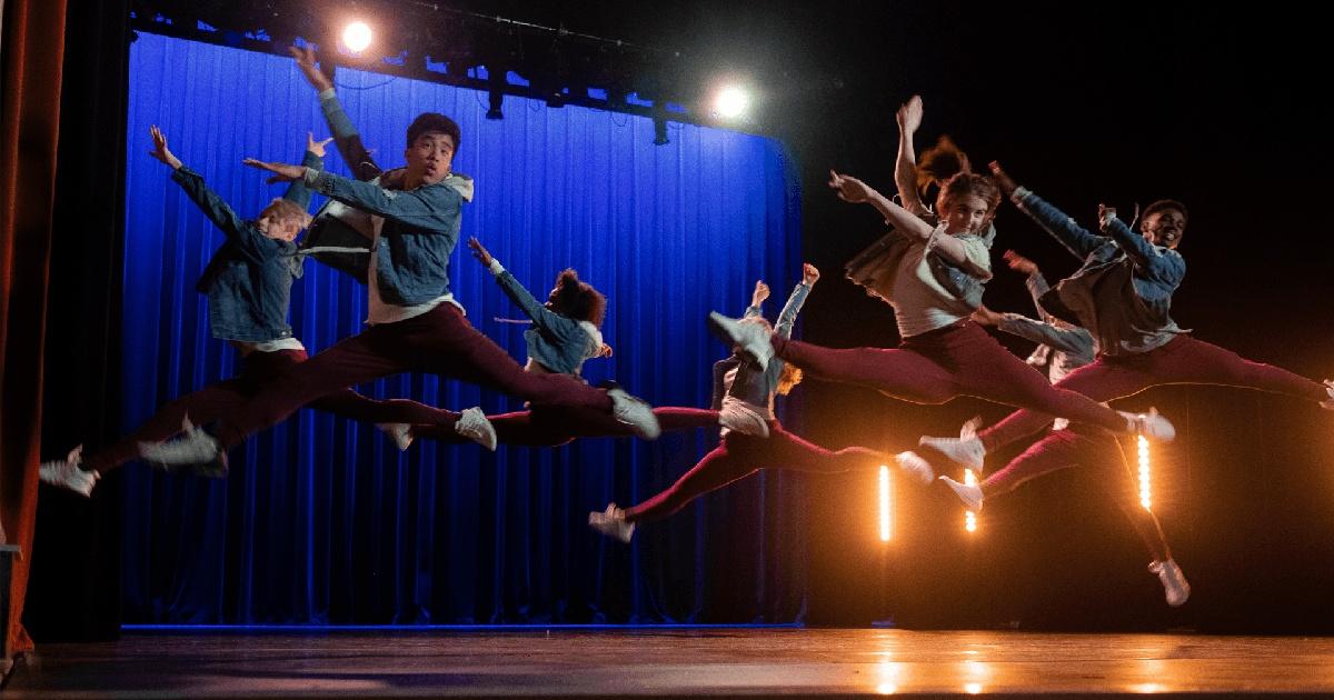 A group of dancers jump together on a stage.