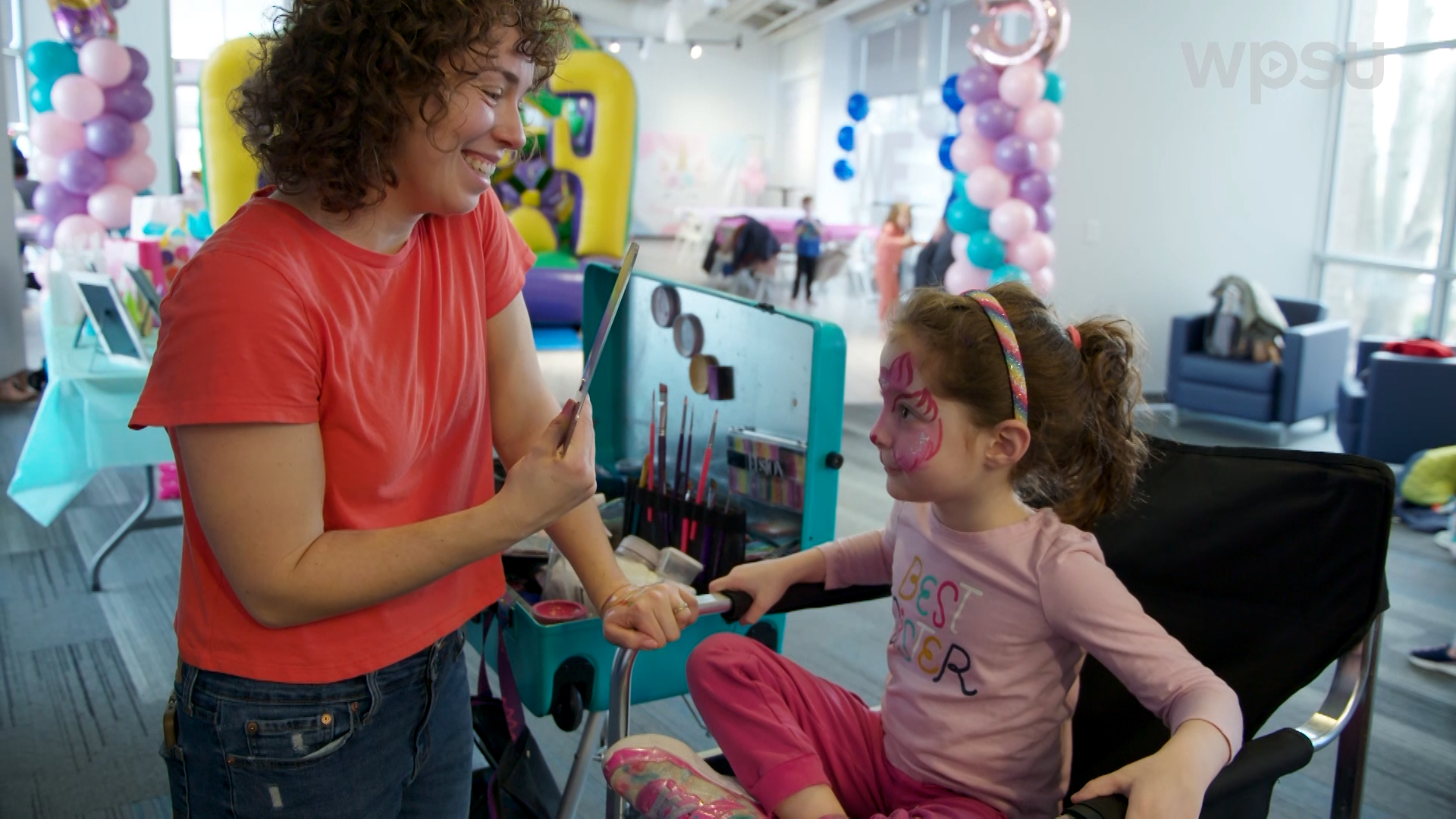 Emily Cooper looks at the completed face paint art on a young girl at a party.