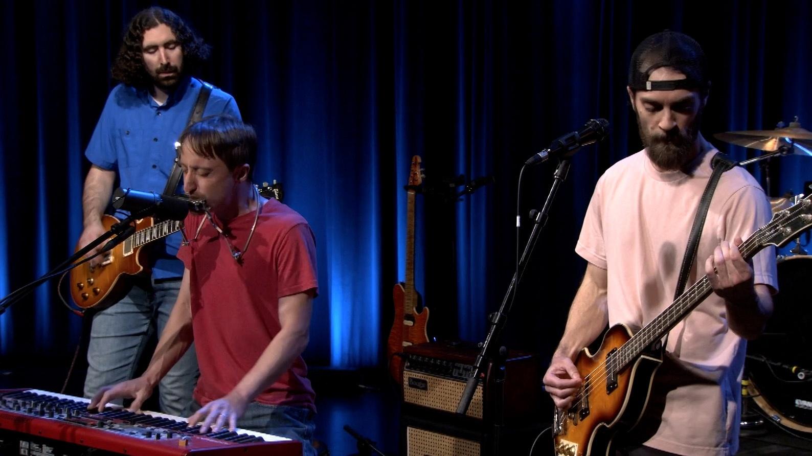 Three musicians playing guitars and keyboard.