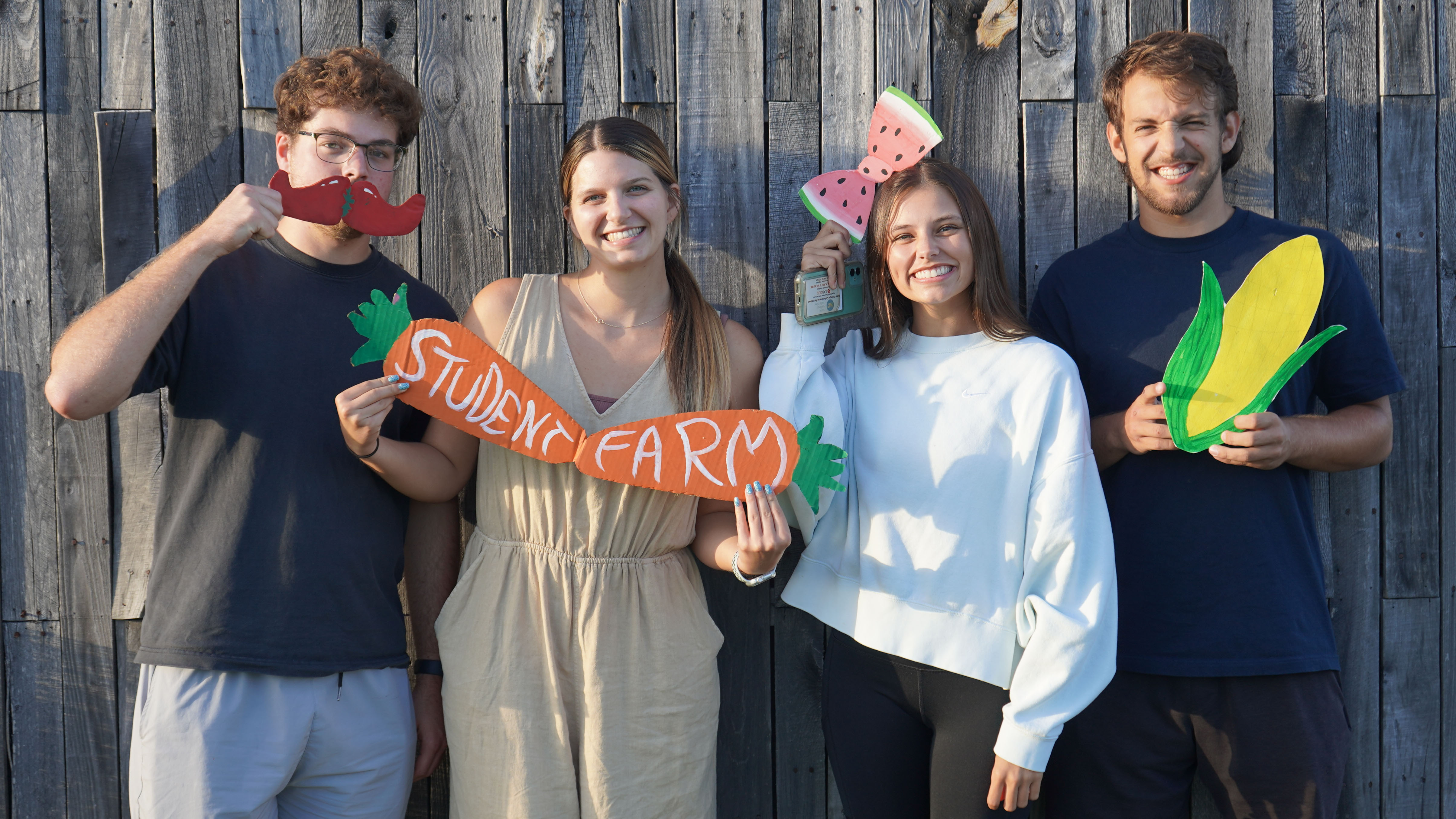Students holding cardboard fruits and vegetables, including a sign that says "student farm."