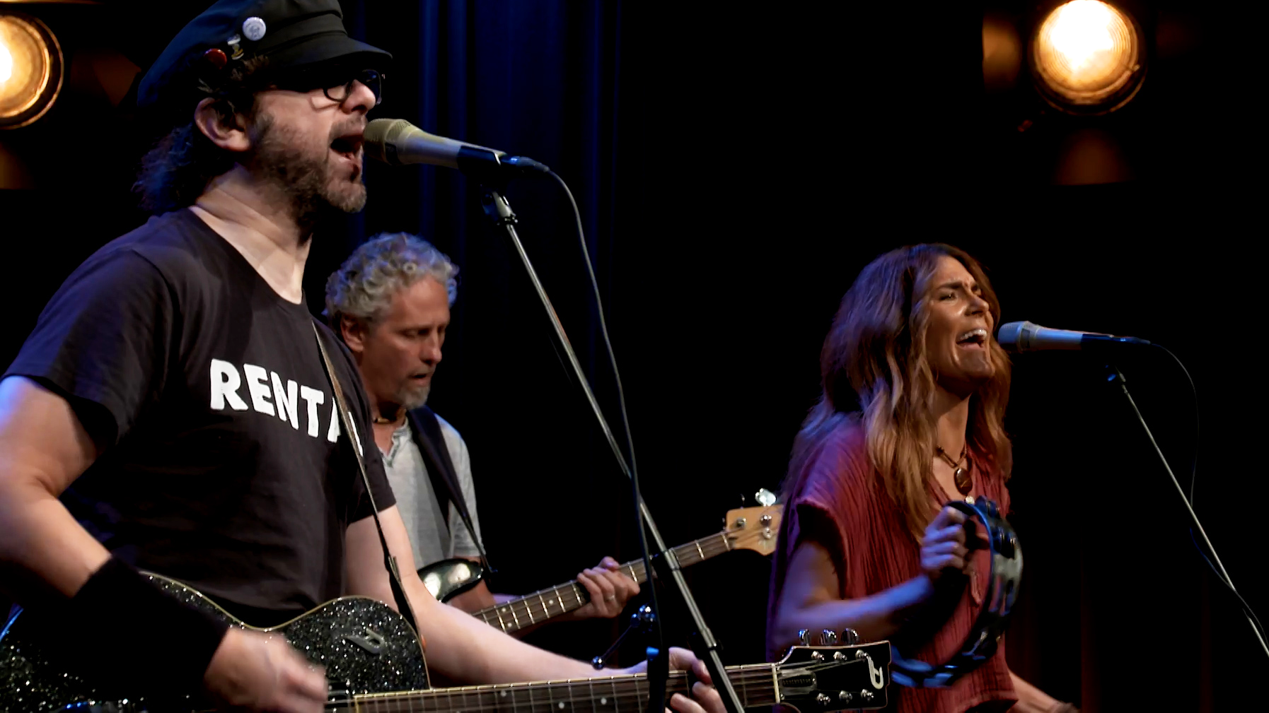 Man playing guitar and singing next to woman playing a tambourine and singing.