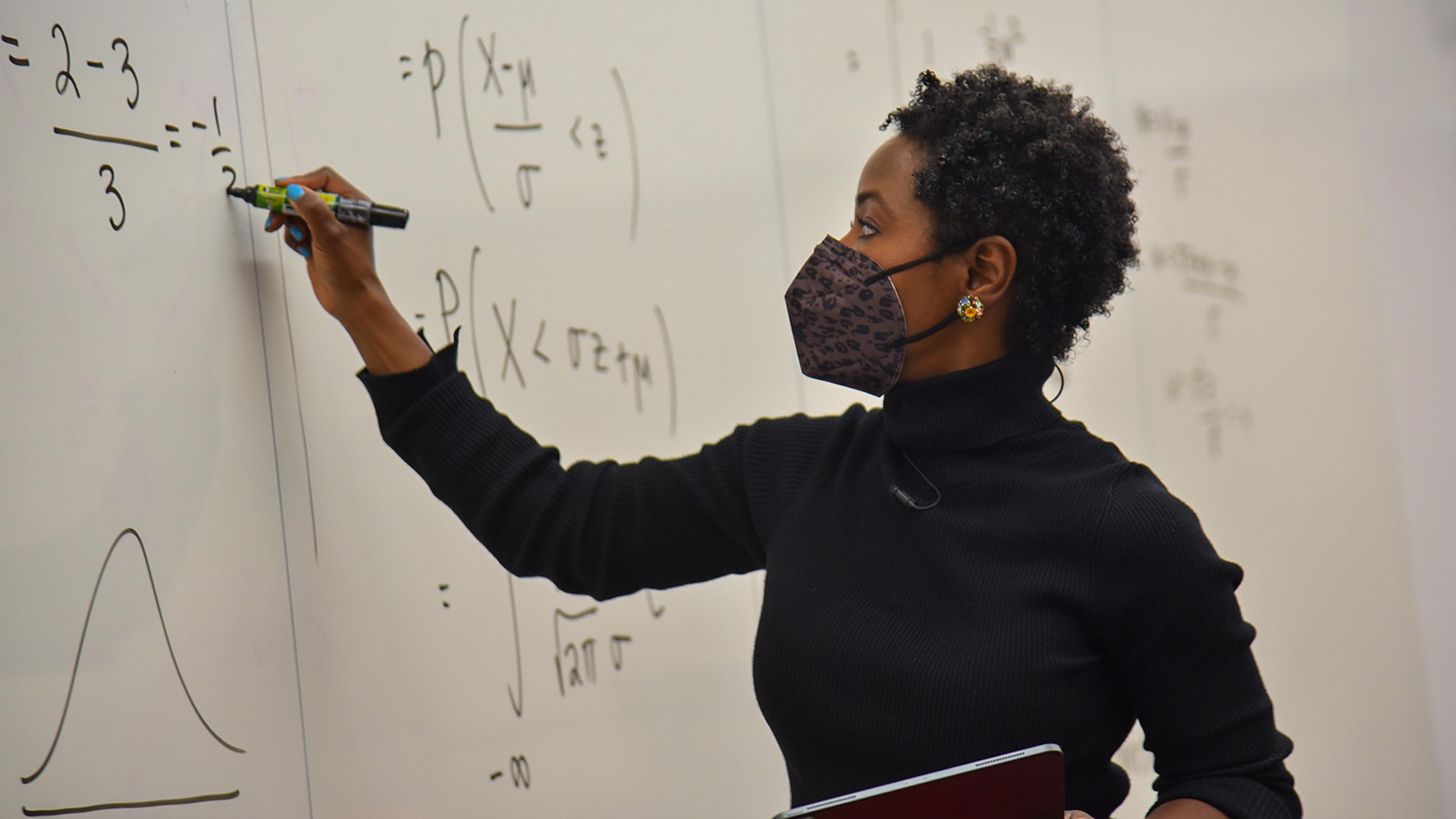 black woman doing match problem on whiteboard wall.
