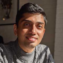 Headshot of man with dark skin and short black hair wearing a gray sweater.
