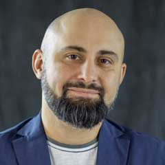 Headshot of bald man with beard wearing white shirt with blue blazer.
