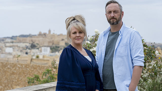 Woman and man standing in front of a scenic European background.