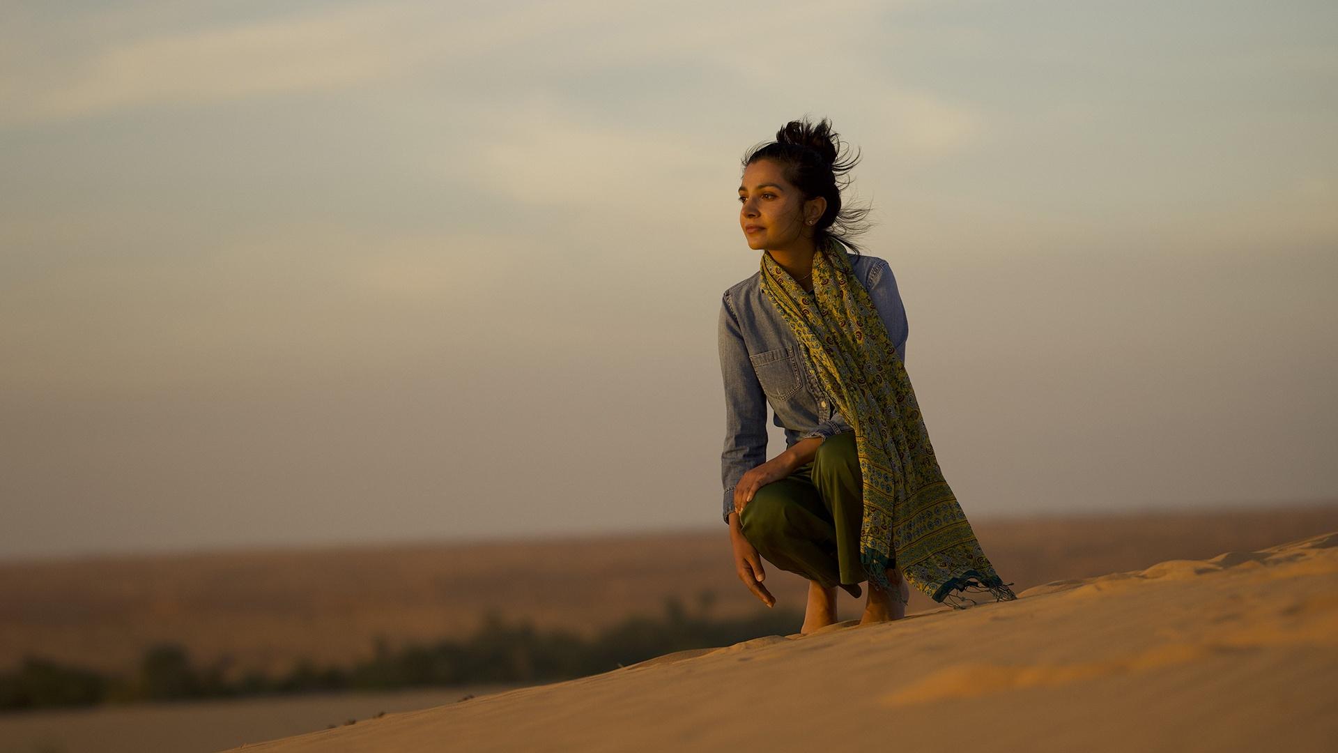 Gulnaz Khan squatting down in an arrid environment.