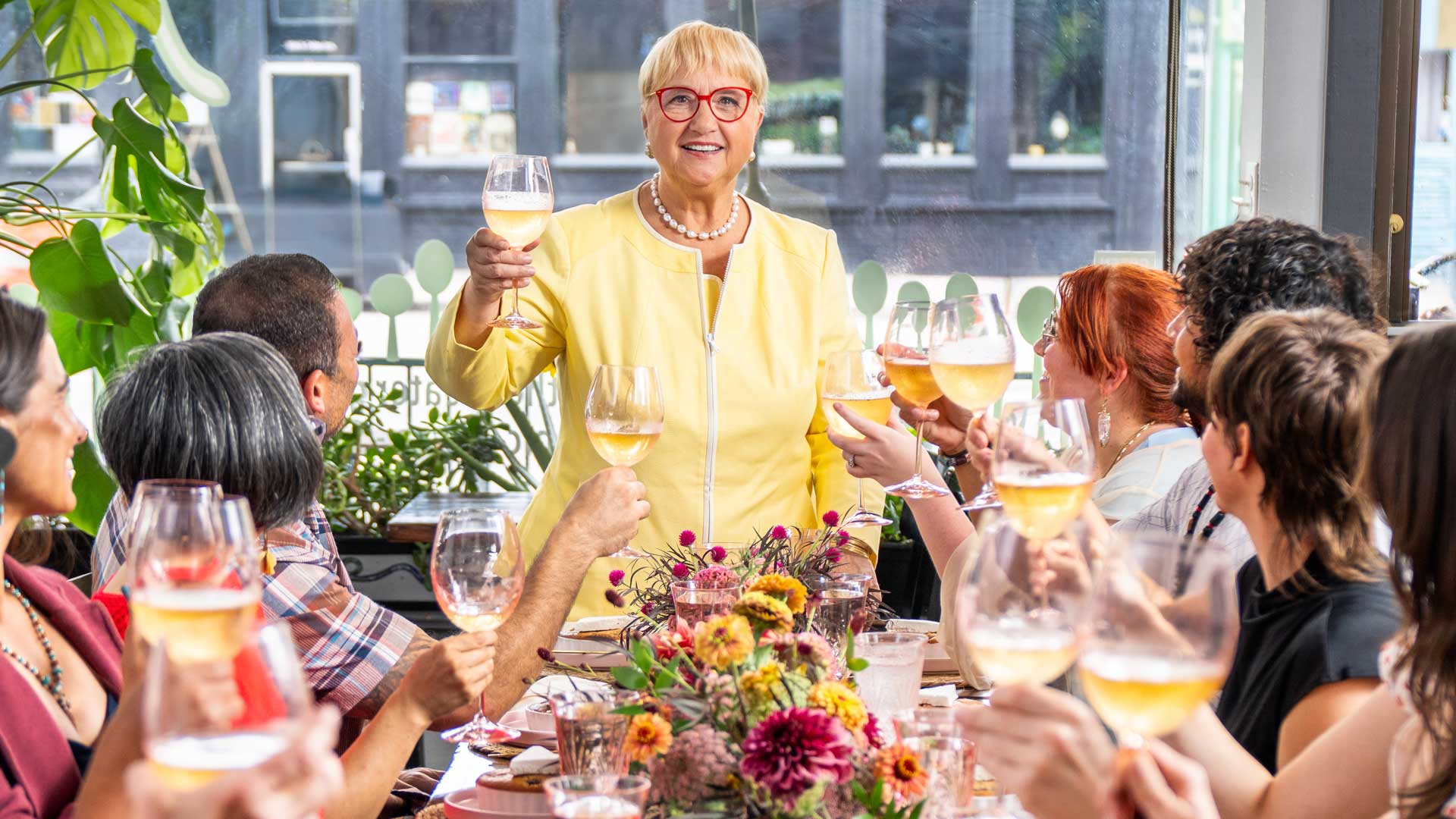 Lidia Bastian leading a toast at a large dinner table.