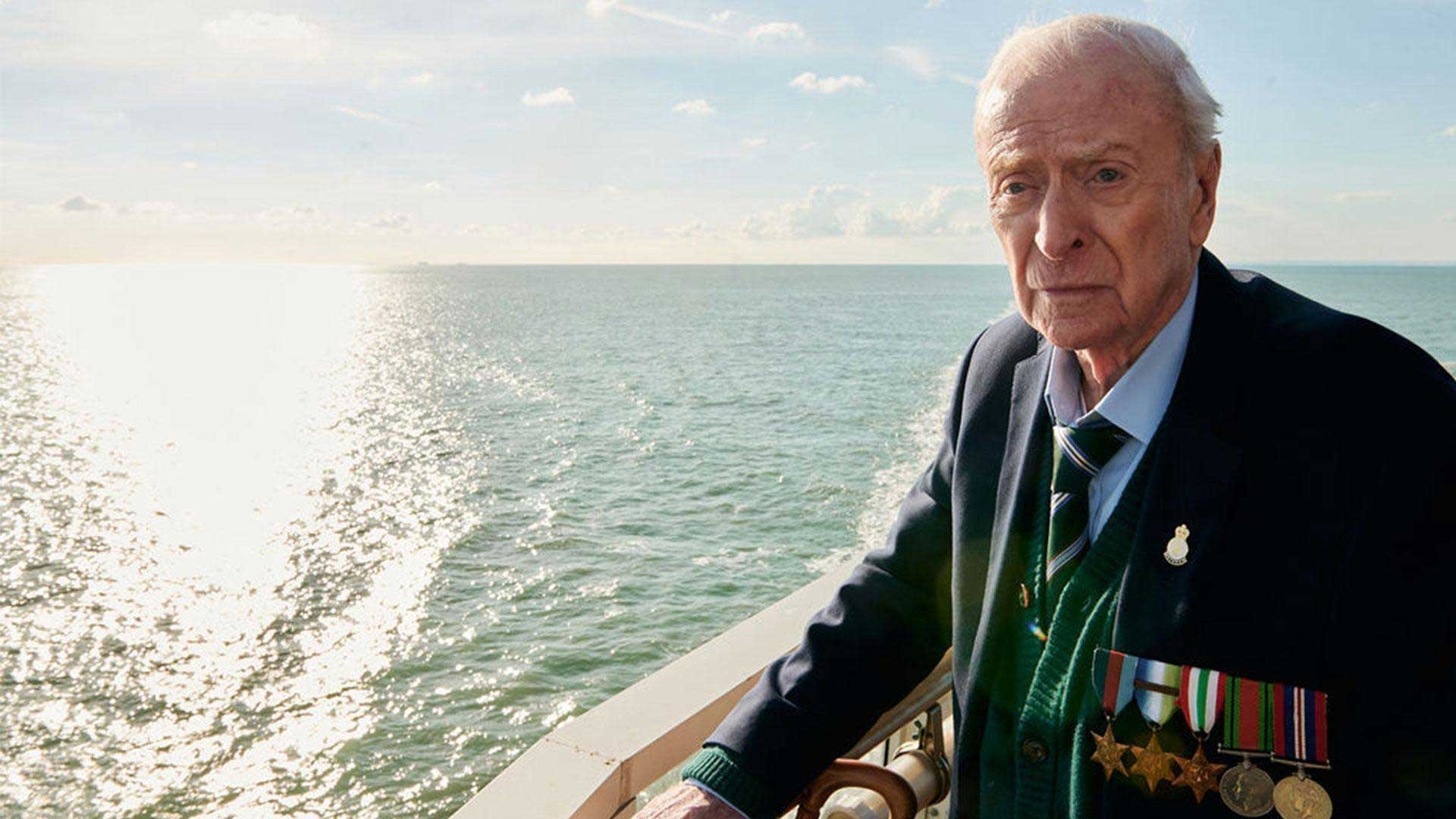 Elderly man standing on boat with open ocean in background.