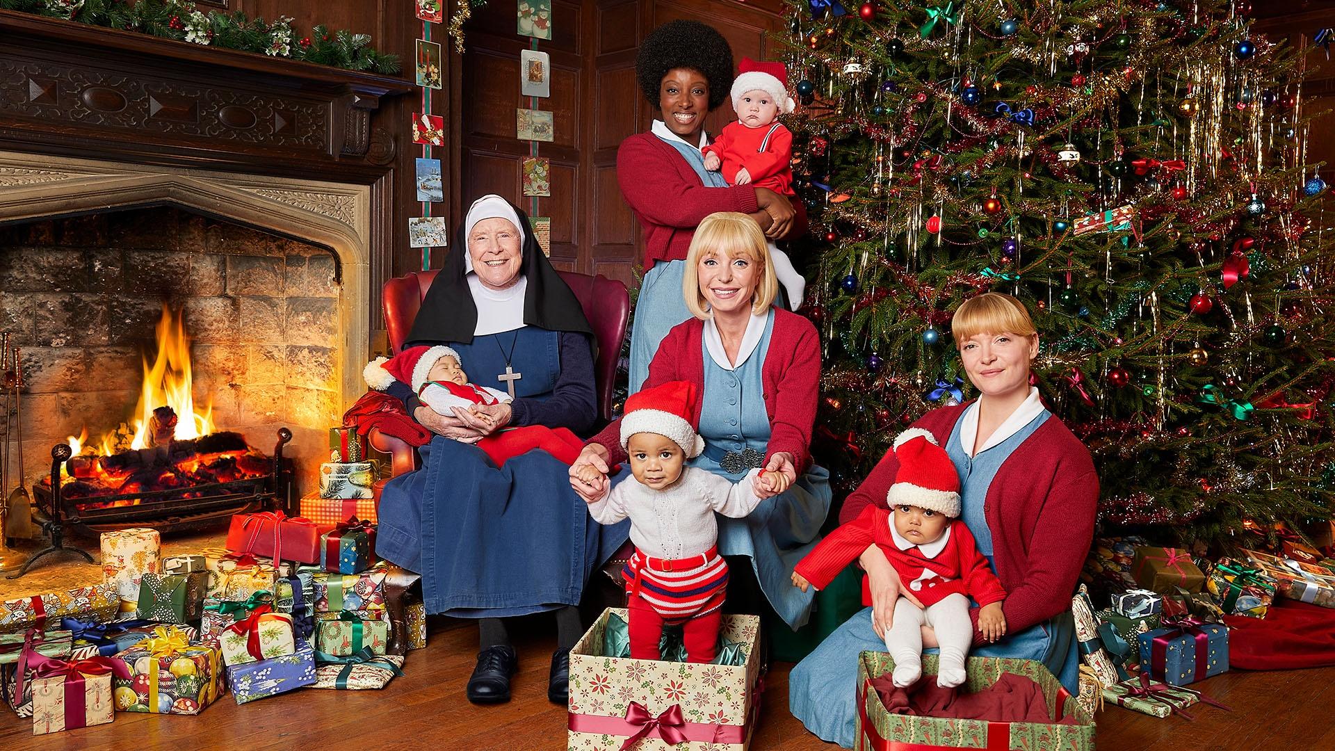 Cast of Call the Midwife in front of a fireplace and Christmas Tree.