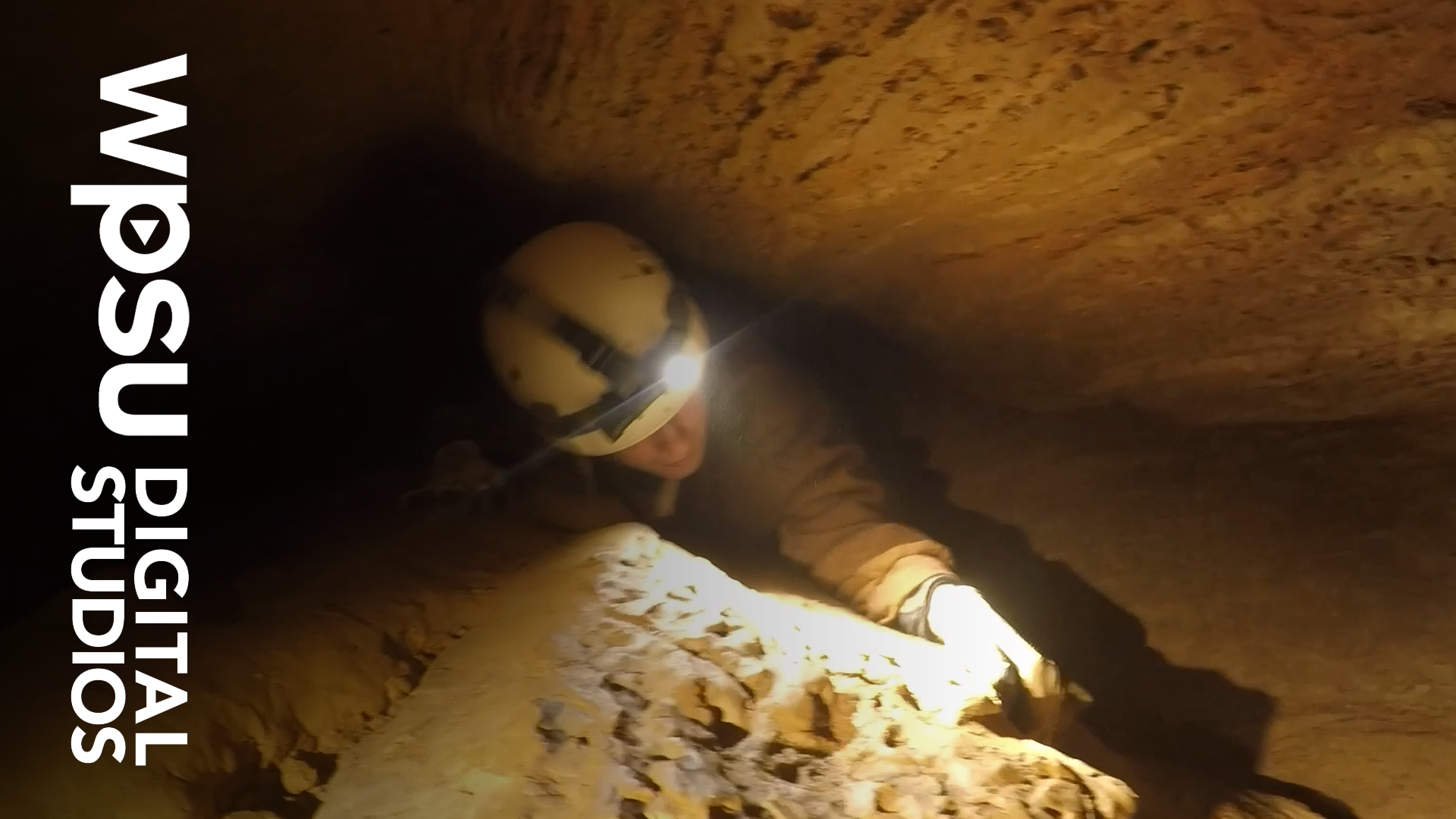 A climber with a hard hat and head lamp inside a cave.