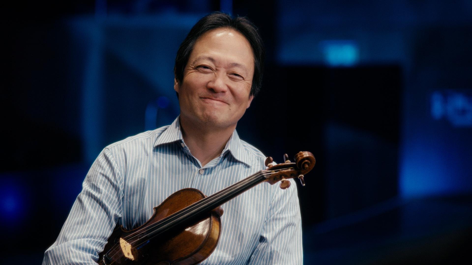Scott Yoo smiling and holding a violin under his arm.