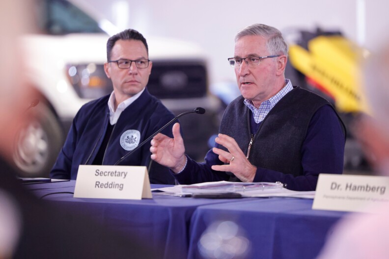 Governor Shapiro sitting behind a table looking at another man.