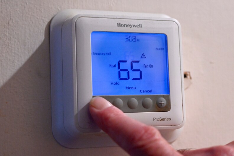 Finger pressing the button on a thermostat.