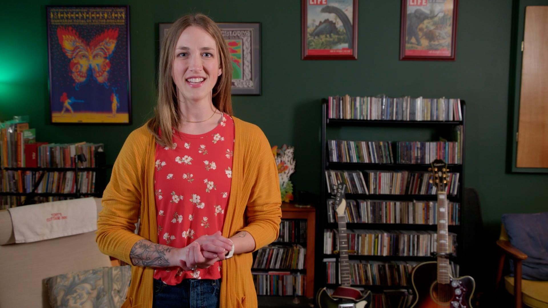 Woman standing in a room with guitars and shelves full of cds.